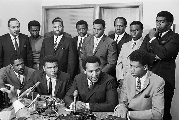 Nation's top Negro athletes gathered for a meeting at the Negro Industrial and Economic Union to hear Cassius Clay's view for rejecting Army induction. News conference shows (front row) Bill Russell, Boston Celtics; Cassius Clay; Jim Brown and Lew Alcindor. Back row (left to right): Carl Stokes, Democratic State Rep.; Walter Beach, Cleveland Browns; Bobby Mitchell, Washington Redskins; Sid Williams, Cleveland Browns; Curtis McClinton, Kansas City Chiefs; Willie Davis, Green Bay Packers; Jim Shorter, former Brown and John Wooten, Cleveland Browns.