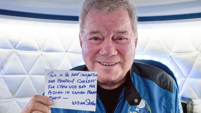 William Shatner holding a hand written sign aboard Blue Origin’s New Shepard rocket.