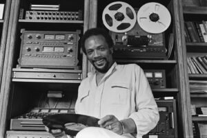 Quincy Jones holding an album in front of his recording equipment.