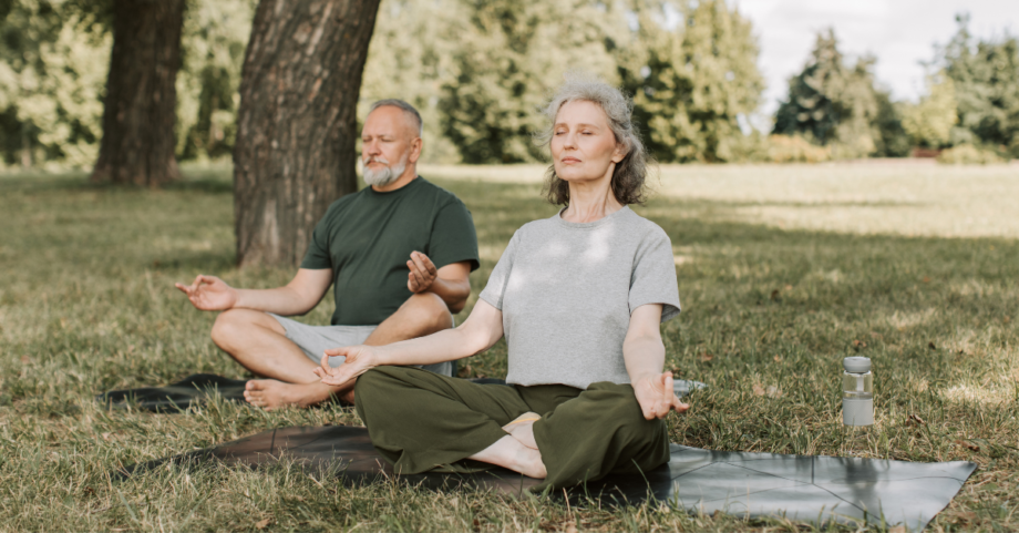 Two older adults practicing gentle seated yoga outdoors, reflecting calm focus, balance, and healthy aging.