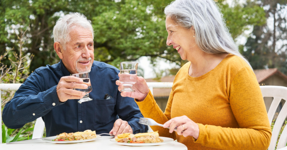 Older couple enjoying a healthy meal and glasses of water together outdoors.
